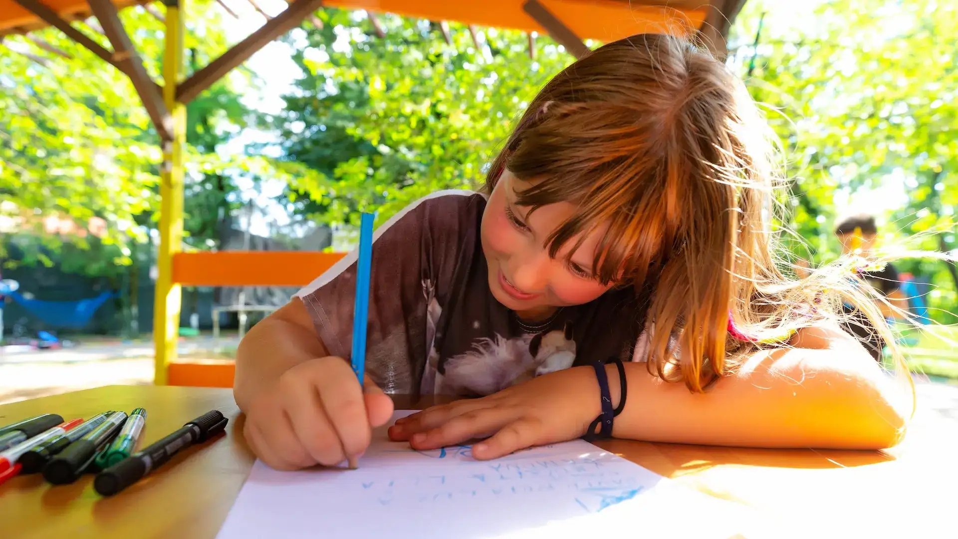 Copil scriind la masă în aer liber la Afterschool Hera Kids din Târgoviște.