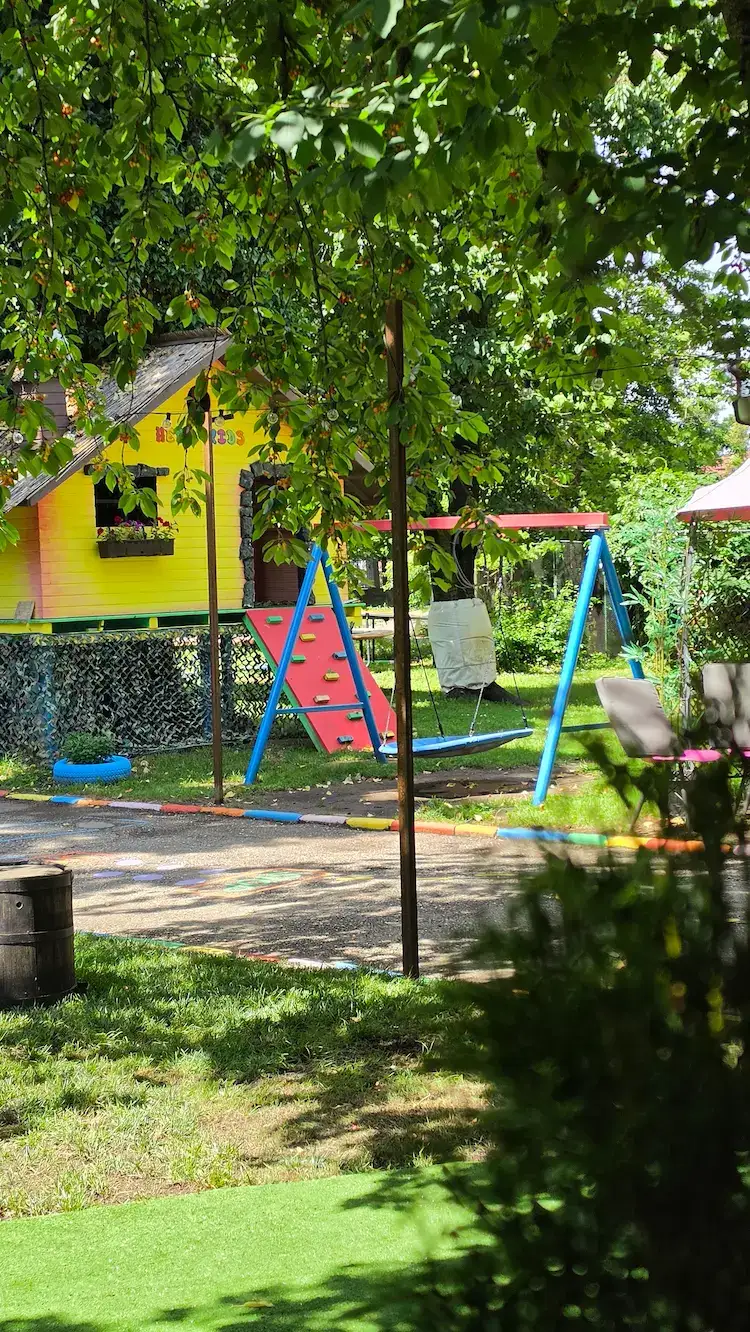 Curtea Hera Kids cu spațiu de joacă, copaci și zone verzi.