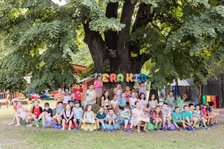 Copii în curtea Hera Kids din Târgoviște, reuniți sub copacul central.