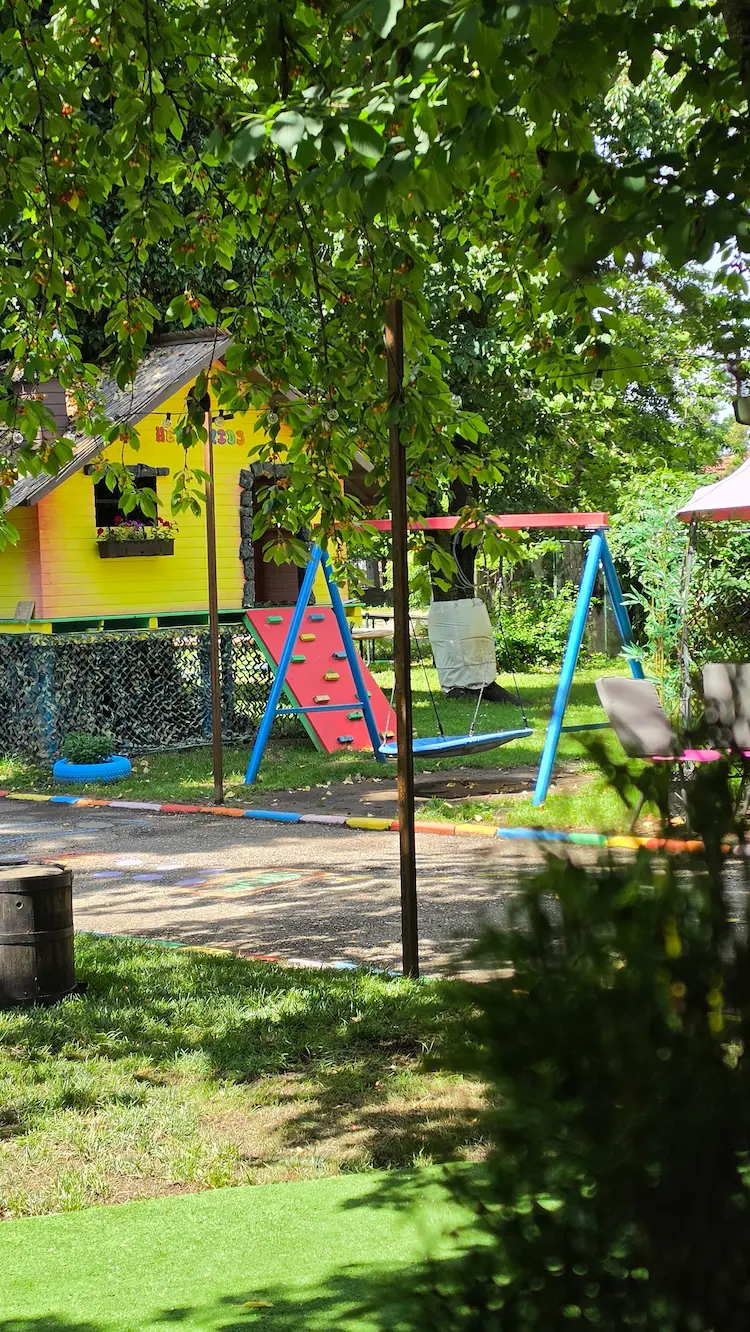 Curtea Hera Kids cu spațiu de joacă, copaci și zone verzi.