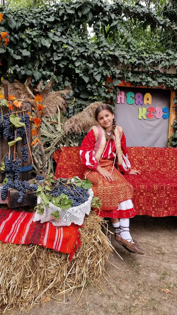 Copil în costum popular la un eveniment Hera Kids cu decor de toamnă și struguri.