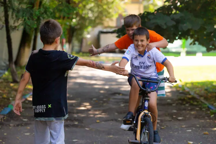Copii jucându-se cu bicicleta în curtea Hera Kids, la Școala de Vară.