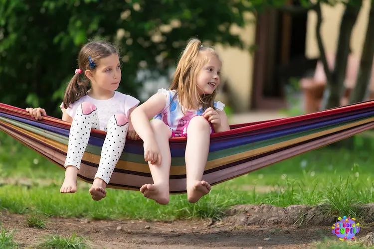 Două fete stând într-un hamac în curtea Hera Kids, la Școala de Vară.